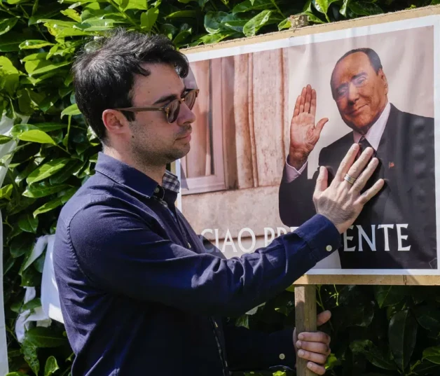 Un hombre se detiene frente a un cartel con la imagen de Silvio Berlusconi en las afueras de la residencia del fallecido ex primer ministro, en Arcore, cerca de Milán, el lunes 12 de junio de 2023.