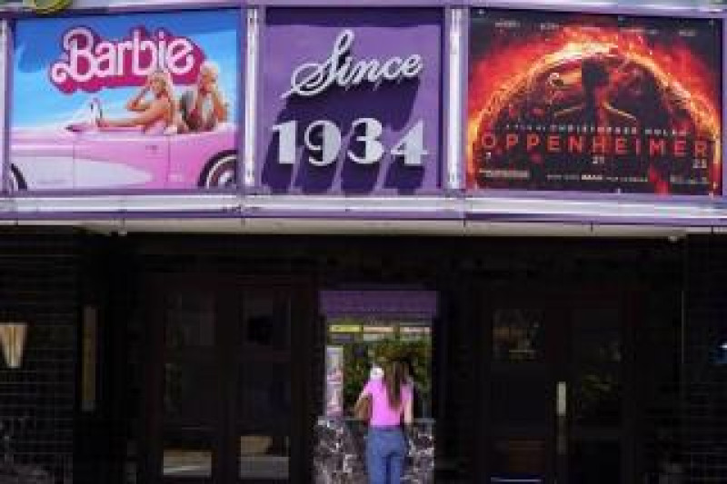 Una persona compra boletos de cine debajo de una marquesina con las películas “Barbie” y “Oppenheimer” en el cine.