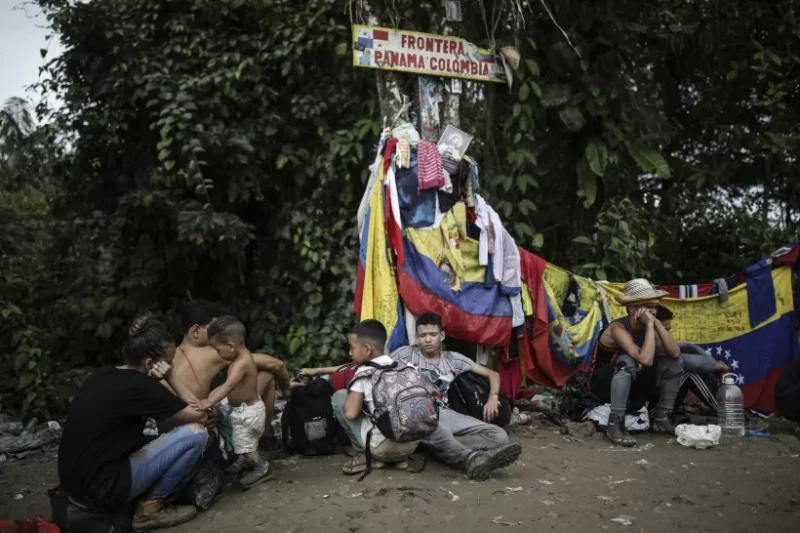 Migrantes sentados bajo un cartel que marca la frontera entre Panamá y Colombia.