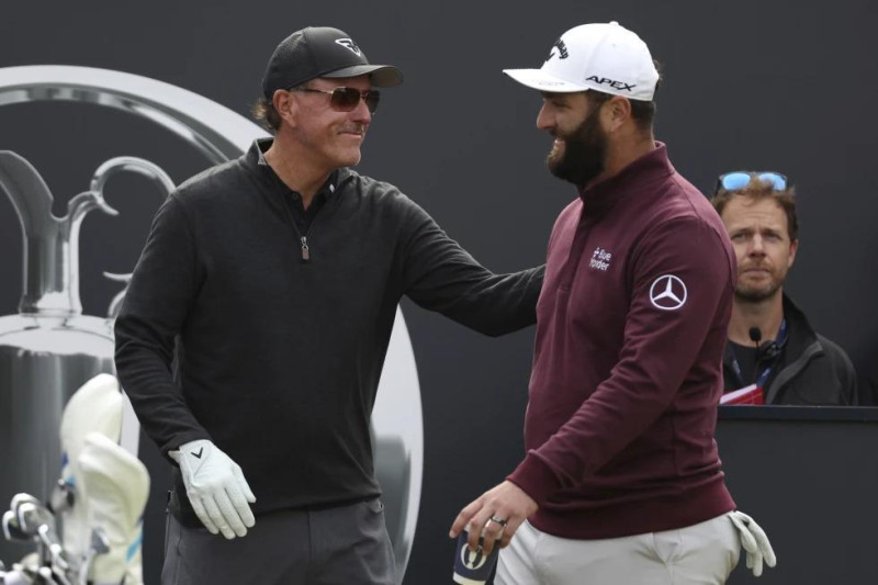 El golfista español Jon Rahm saluda al estadounidense Phil Mickelson en el primer tee durante una ronda de práctica para el Abierto Británico de golf.