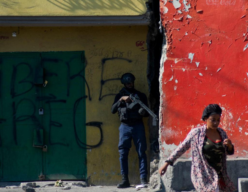 Una mujer pasa frente a un agente de policía armado que vigila una calle tras otra jornada de violencia de bandas en Puerto Príncipe, Haití, el 22 de marzo de 2024