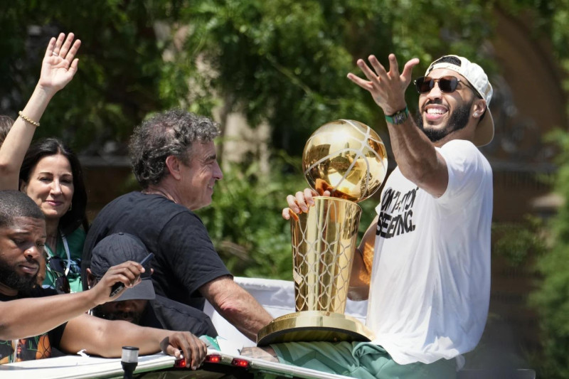 ayson Tatum, de los Boston Celtics, a la derecha, y el propietario de los Celtics, Wyc Grousbeck, en el centro, celebran su campeonato de baloncesto de la NBA con un desfile.