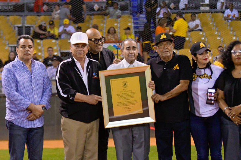 Mendy López recibe de Víctor García Sued y Wiston Llenas la placa de reconocimiento tras el bautismo con su nombre de la cabina de radio del estadio Cibao de Santiago.