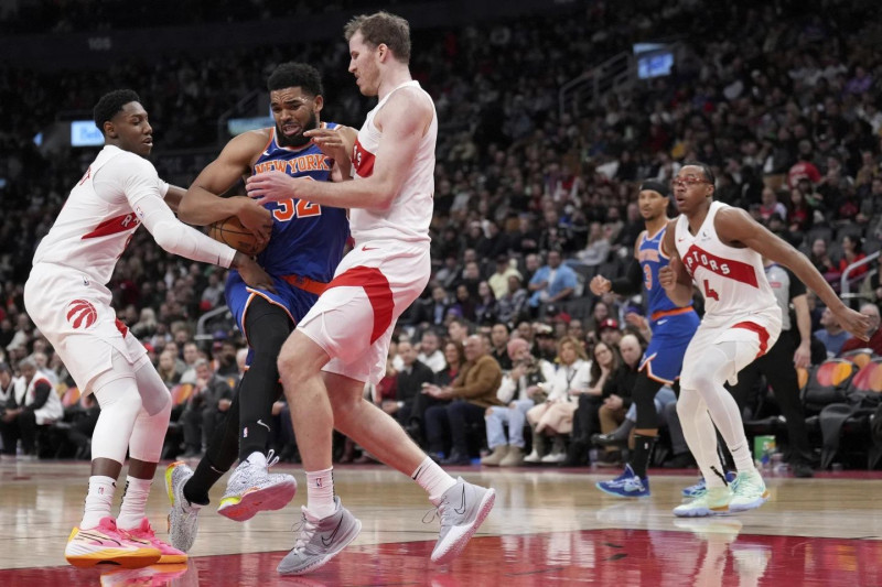 Karl-Anthony Towns,de los Knicks, protege el balón ante la defensa de Jacob Poeltl y R.J. Barrett, de los Raptors, en acción del partido en el balocesto de la NBA.