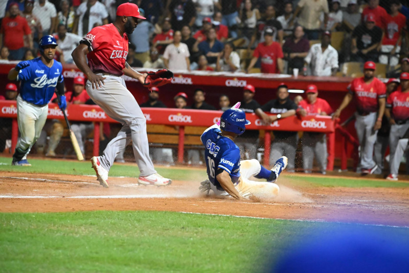 Gustavo Núñez anota la carrera de la victoria de los Tigres del Licey en entradas extras frente al pitcher Henry Sosa de los Leones del Escogido