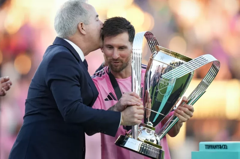 Lionel Messi, de Inter Miami, sostiene el trofeo de campeón de la MLS y recibe un beso de Jorge Mas, dueño del equipo, tras la victoria ante Vancouver Whitecaps en la final.