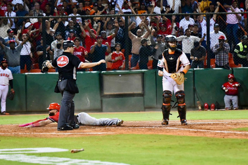 Michael De La Cruz se desliza en la goma para anotar la carrera del triunfo para los Leones luego de que Yairo Muñoz haga un disparo errado a la inicial.