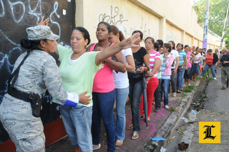 Mayo 2012. Revisión. Está prohibido a los ciudadanos ingresar al recinto de votación con aparatos electrónicos, cartera o bultos, armas de fuego o blancas, identificación de algún partido político, marcadores u otros objetos. En esta fotografía se observa una policía militar revisando a los ciudadanos, antes de permitir el acceso al centro de votación.