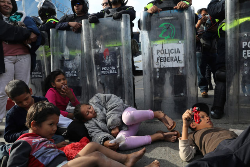 Acción. Niños migrantes descansan frente a una fila de policías mexicanos en uniformes de faena, cuando trataban de cruzar la frontera en Tijuana.