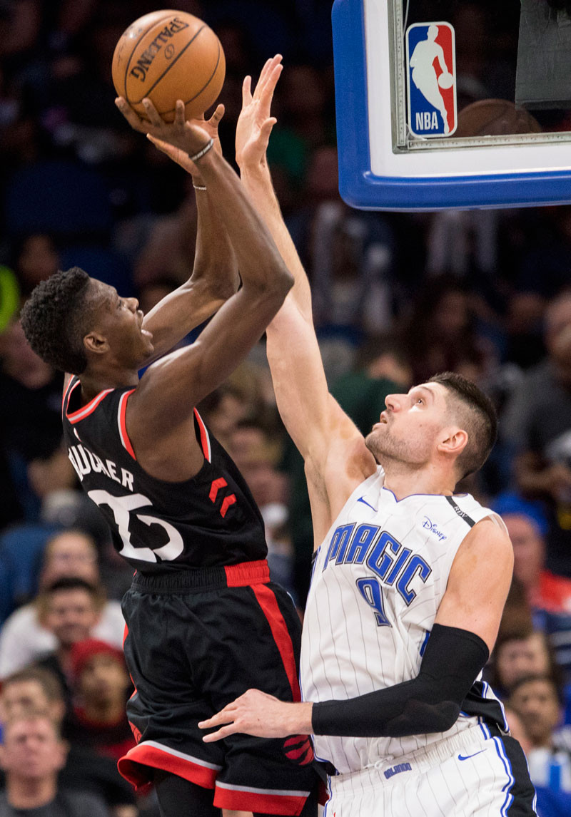 Chris Boucher (25), de Toronto, trata en encestar un canasto sobre la defensa del centro de los Magic de Orlando Nikola Vucevic durante la segunda mitad del partido de anoche en el baloncesto de la NBA.