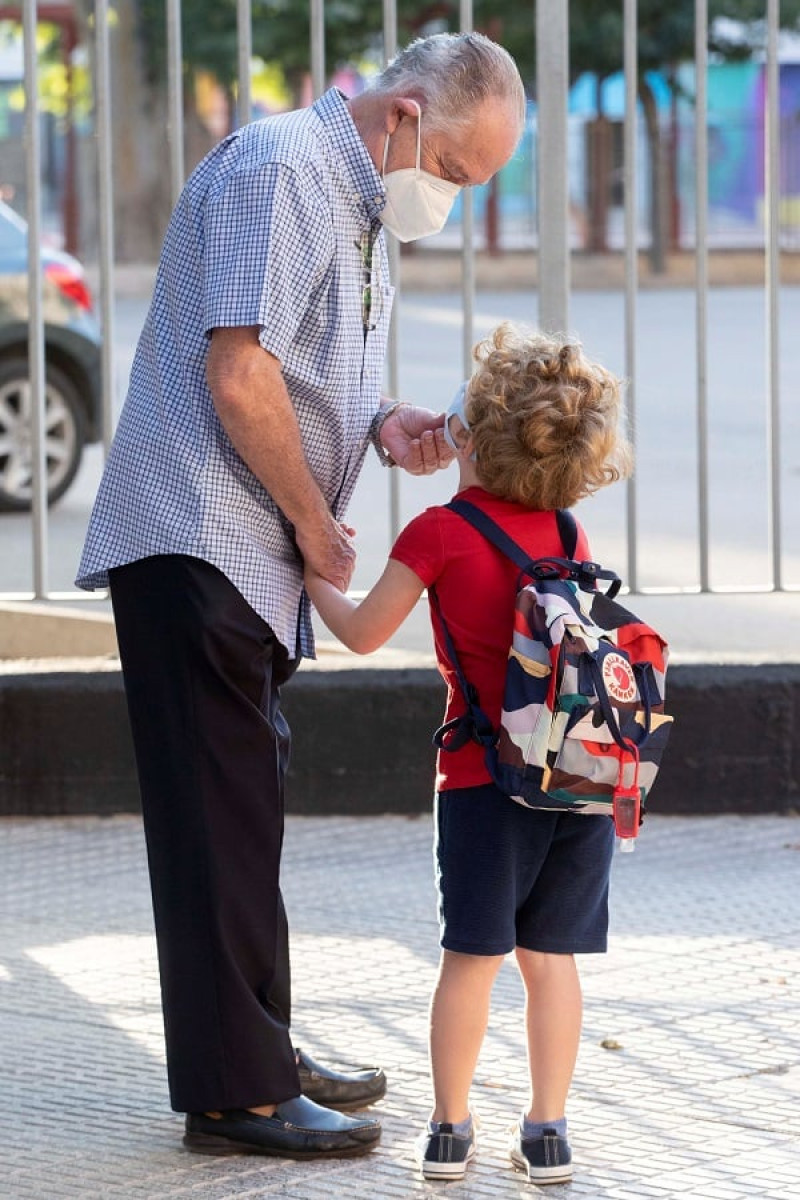 Un abuelo coloca bien la mascarilla de su nieto antes de entrar al colegio. EFE/Marcial Guillén