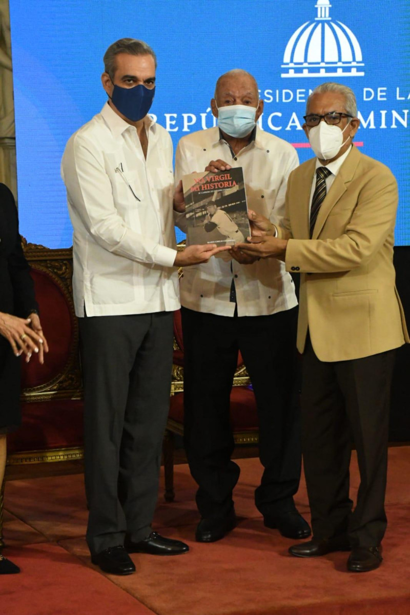 El presidente Luis Abinader y Osvaldo Virgil reciben de manos del periodista Mario Emilio Guerrero, un ejemplar de su libro, Yo, Virgil, Mi Historia.