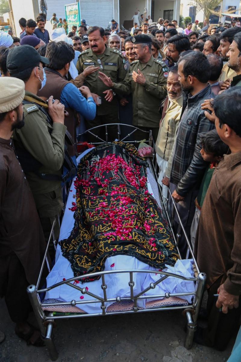 Familiares, lugareños y policías se paran cerca de un ataúd que contiene el cuerpo de un hombre durante su funeral en el distrito de Khanewal el 13 de febrero de 2022, quien fue asesinado después de que una turba enfurecida lo apedreó hasta la muerte. Foto: Shahid Saeed Mirza/AFP.
