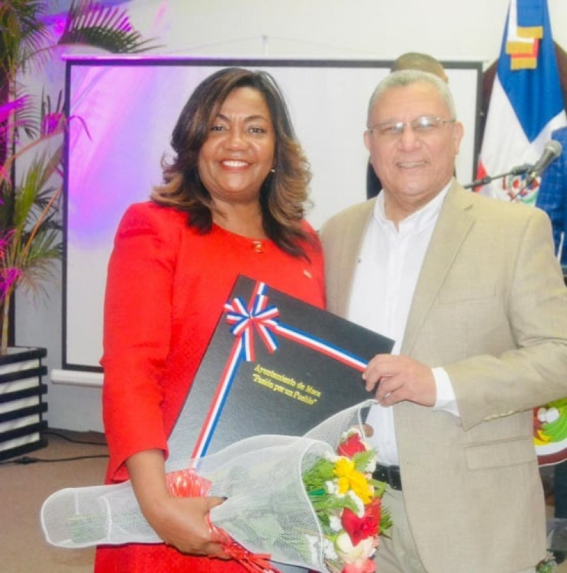 El alcalde de Moca, Miguel Ángel Guarocuya Cabral entrega a Amarilys Durán el pergamino 'visitante distinguida'.