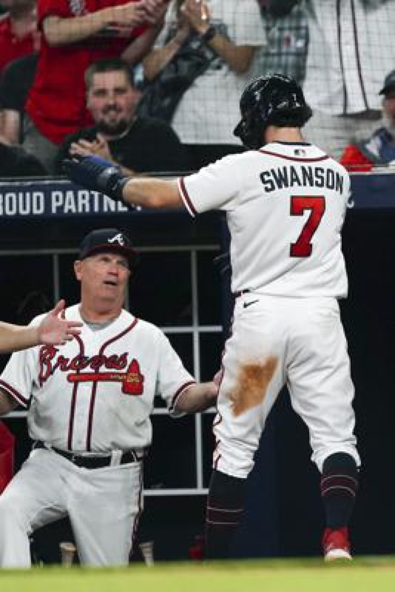 Dansby Swanson, de los Bravos de Atlanta, es felicitado por el manager Brian Snitker, luego de anotar en un error de los Filis de Filadelfia.