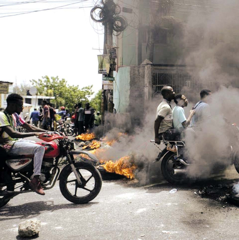 Un mototaxista lleva a sus clientes más allá de una barricada en llamas colocada por
taxistas para protestar por la escasez de combustible en Puerto Príncipe, ayer. AP