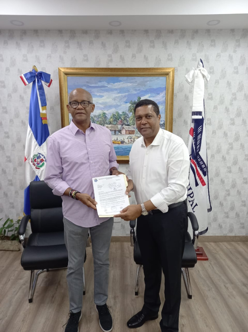 El licenciado Víctor D´ Aza mientras recibía de manos de José –Yeye—Aybar la certificación que da cuenta que la Copa Liga Municipal Dominicana será disputada en la justa atlética.