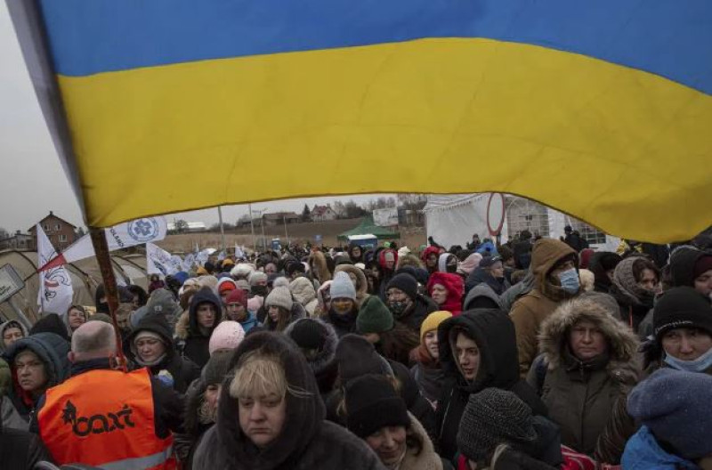 El voluntario ucraniano Oleksandr Osetynskyi, de 44 años, sostiene una bandera ucraniana y dirige a cientos de refugiados tras huir de Ucrania y llegar al cruce fronterizo en Medyka, Polonia, el lunes 7 de marzo de 2022. La guerra ha sido una catástrofe para Ucrania y desencadenado una crisis para todo el planeta. (AP Foto)