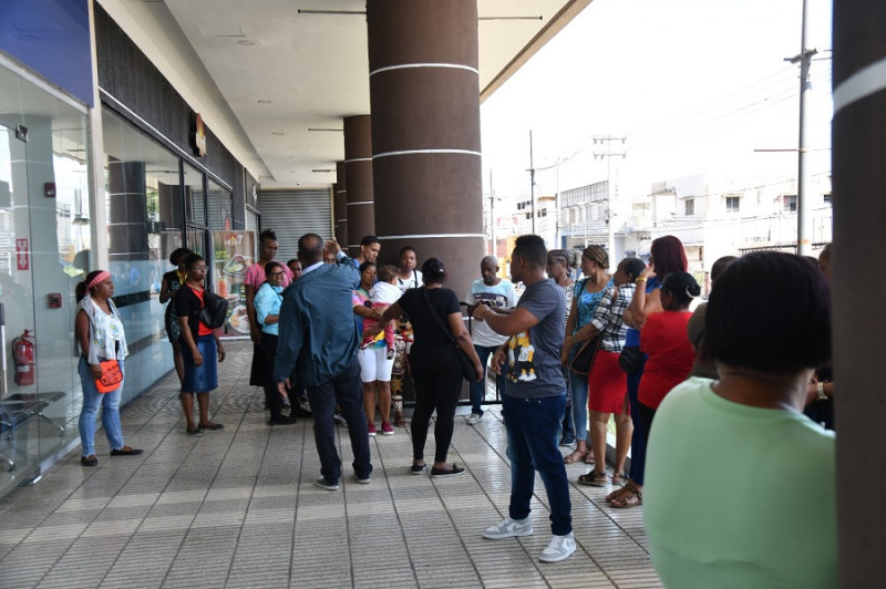 Un grupo de personas espera a las afueras de la plaza comercial Sambil para ser atendidos en la oficina gubuernamental Punto Gob, entre ellos una mujer con una niña en brazos.