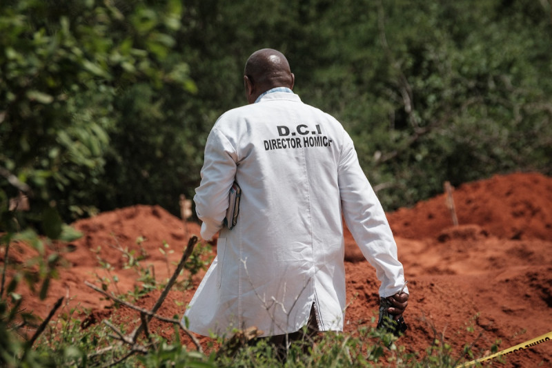 Un oficial de la Dirección de Investigaciones Criminales (DCI) de Kenia camina junto al terreno excavado en la fosa común en Shakahola, en las afueras de la ciudad costera de Malindi, el 25 de abril de 2023.
