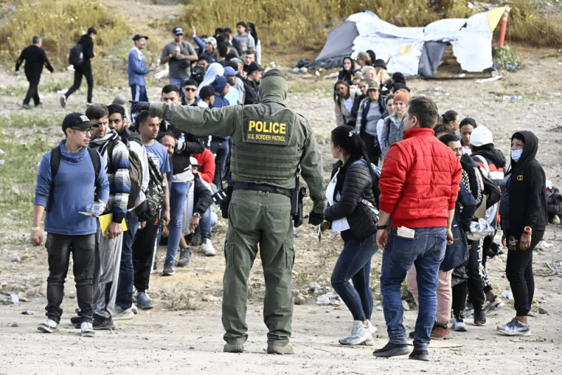 Un agente de la Patrulla Fronteriza da indicaciones a solicitantes de asilo para que esperen en la frontera de Estados Unidos con México, cerca de Tijuana, México, el lunes 8 de mayo de 2023, en San Diego.