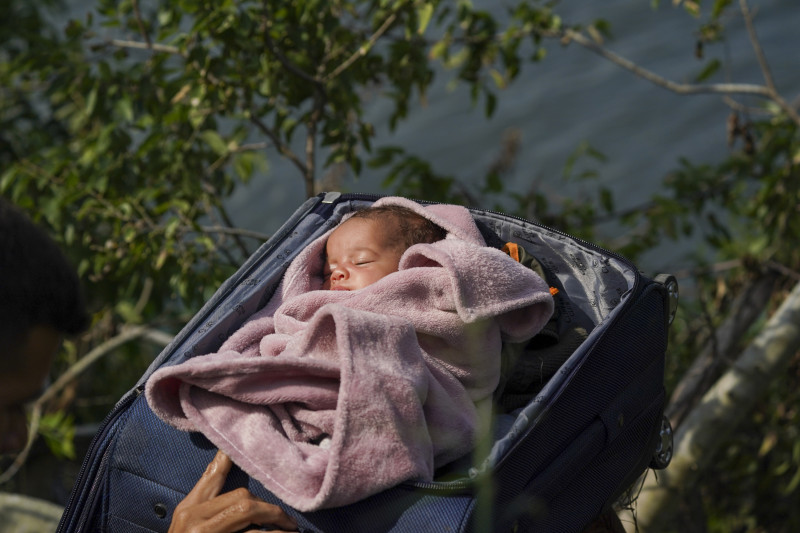 Migrantes cruzan el río Bravo hacia Estados Unidos con un bebé dentro de una maleta abierta, en esta fotografía tomada desde Matamoros, México, el miércoles 10 de mayo de 2023.