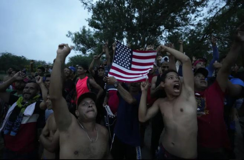 Migrantes venezolanos ondean una bandera estadounidense frente a un helicóptero de televisión que sobrevolaba la zona en Matamoros, México, el viernes 12 de mayo de 2023.