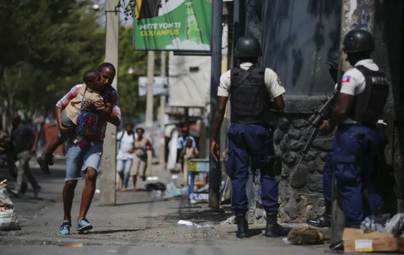Un padre carga a su hijo luego de pasar por él a la escuela en medio de un operativo policial contra pandillas en la capital haitiana.