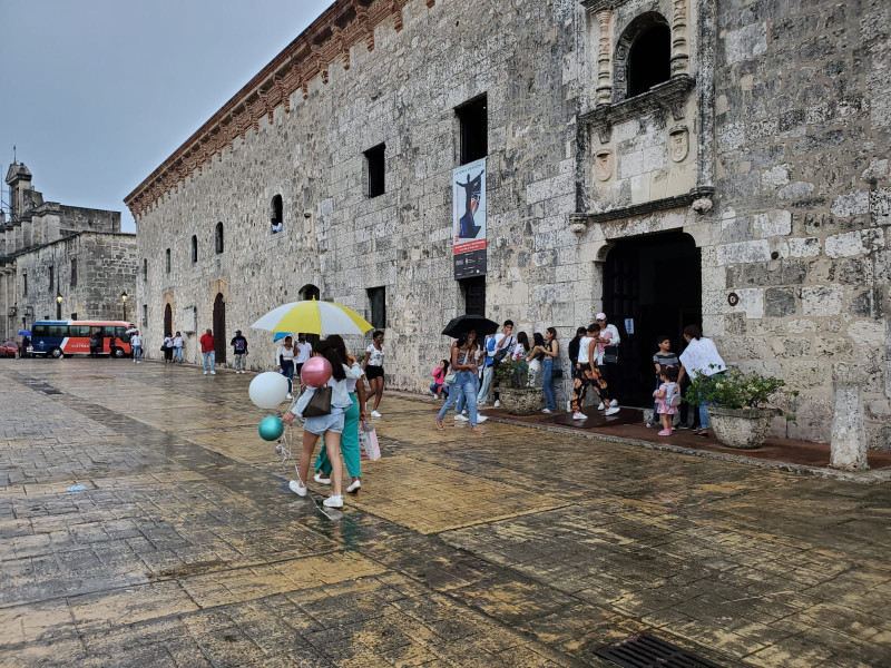 Transeúntes con paraguas caminan por el Museo de las Casas Reales, mientras que otros se reúnen en la puerta para entrar.