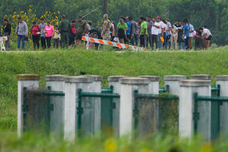 Migrantes hablan con funcionarios junto a una carretera cerca de Río Grande tras cruzar la frontera entre Texas y México, el jueves 11 de mayo de 2023 en Brownsville, Texas.