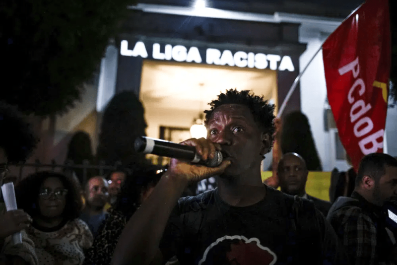 Delante de un mensaje proyectado en la fachada del consulado de España en Sao Paulo, un manifestante habla durante una protesta contra las expresiones racistas lanzadas a Vinícius Júnior, el martes 23 de mayo de 2023.