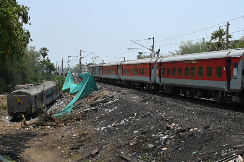 Un tren de pasajeros de larga distancia pasa junto a un vagón dañado mientras circula por la vía recién restaurada en el lugar del accidente de una reciente colisión de tres trenes cerca de Balasore, a unos 200 km (125 millas) de la capital del estado, Bhubaneswar, en el estado oriental de Odisha, el 5 de junio de 2023.