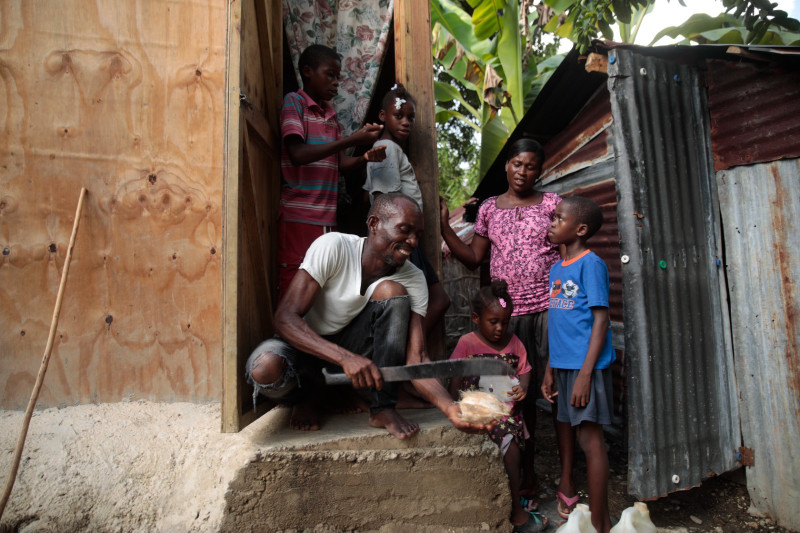 Mackenson Victor abre un coco para su hija, Manouchi Victor, el centro al frente, y sus hijastros, Myson Veillard, arriba a la izquierda, Routcheland Veillard, arriba, segunda desde la izquierda, y Dabens Veillard, al frente a la derecha, ante la mirada de su pareja, Renèse Estève.