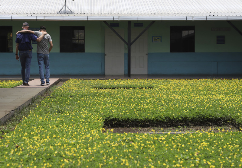 El pastor estadounidense Kenton Moody, a la izquierda, camina abrazado con un joven que estuvo en prisión por formar parte de una pandilla, en un descanso en el jardín del centro de rehabilitación de "Vida Libre", en Santa Ana, El Salvador, el sábado 29 de abril de 2023.