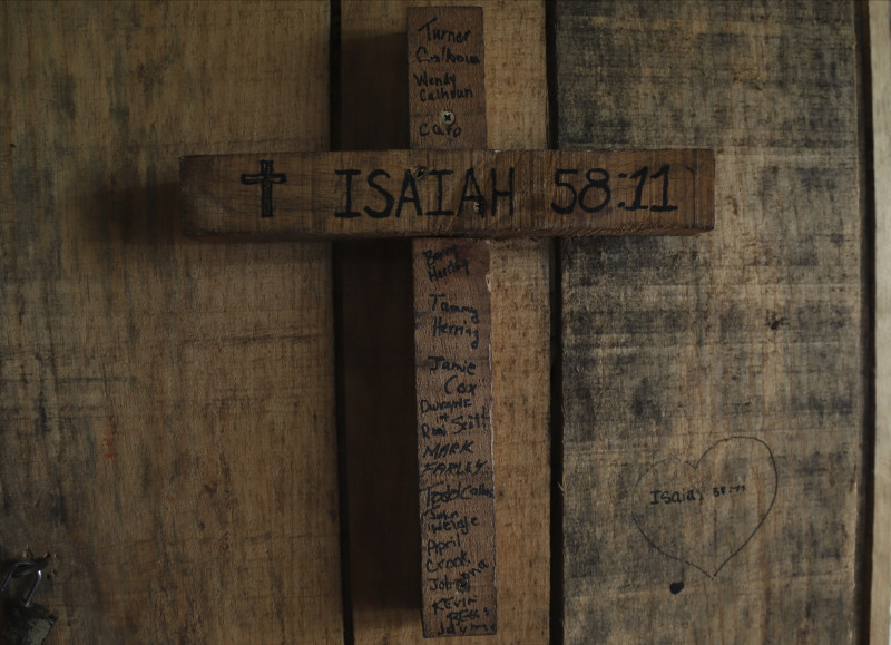 Una cruz de madera tiene grabado un verso bíblico y el nombre de miembros de la iglesia estadounidense que construyeron la casa en la que está colgada la cruz, en una zona antes controladas por las pandillas, en Santa Ana, El Salvador, el sábado 29 de abril de 2023.