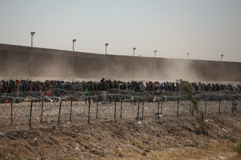 ARCHIVO - Migrantes alineados entre una valla con alambre de púas y el muro fronterizo entre Estados Unidos y México, visto desde Ciudad Juárez, México, el 9 de mayo de 2023.