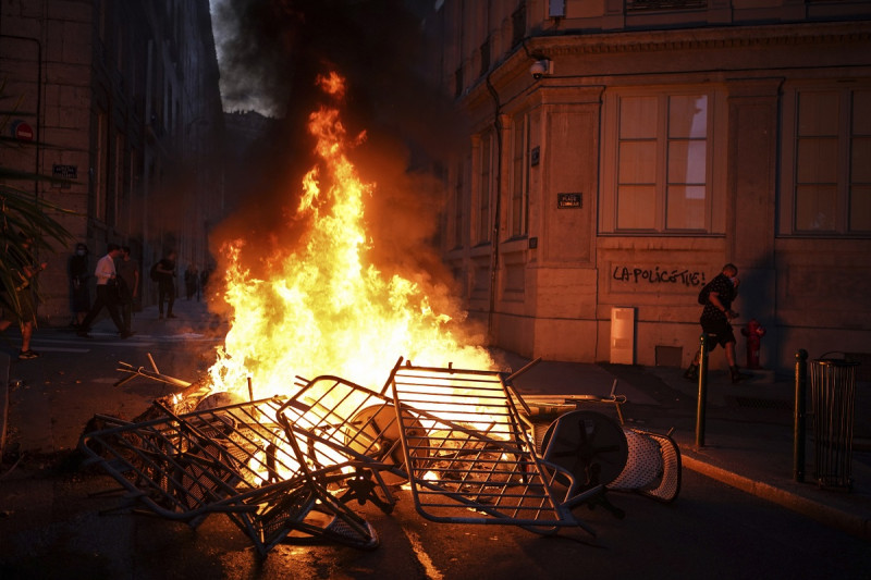 Un hombre pasa frente a una pared iluminada por una barricada en llamas en la que está escrito "La policía mata" en el centro de Lyon, en el centro de Francia, el viernes 30 de junio de 2023.