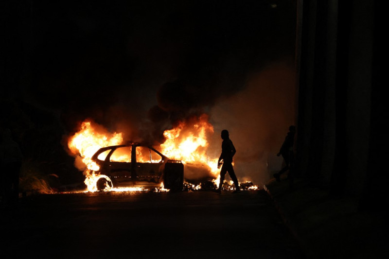 Manifestantes pasan junto a un coche en llamas durante los enfrentamientos con la policía en Le Port, en la isla francesa de La Reunión, en el océano Índico, el 30 de junio de 2023, tres días después de que un joven de 17 años recibiera un disparo en el pecho a quemarropa por parte de la policía en Nanterre, un suburbio del oeste de París