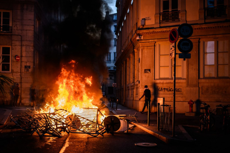 El humo sale de una hoguera cerca de un grafiti que dice "La policía mata" durante los enfrentamientos con la policía en las calles de Lyon, sureste de Francia, el 30 de junio de 2023, tres días después de que un niño de 17 años recibiera un disparo en el pecho.