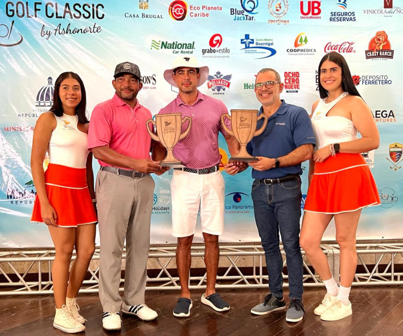 Raúl Linares (centro) recibe el trofeo de Mejor Score Gross Overall del Puerto Plata Golf Classic by ASHONORTE, honor que ganó jugando junto a Juan Marcos Yunén. Entregan Carlos Rodolí, Luis Caraballo, y las modelos ASHONORTE.
