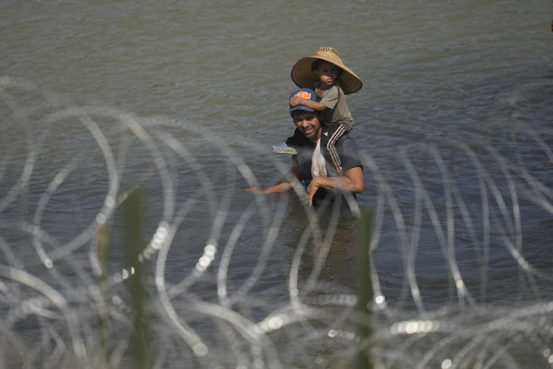 Un migrante cruza el río Bravo con un niño sobre sus hombros en un intento por llegar a Estados Unidos desde México.