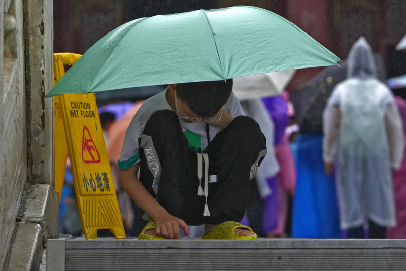 Un niño se protege de la lluvia con un paraguas mientras revisa un celular, en el piso de la Ciudad Prohibida de Beijing, el 13 de julio de 2023.
