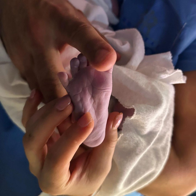Las manos de Carlos Rivera y Cynthia Rodríguez agarrando uno de los pies de su bebé