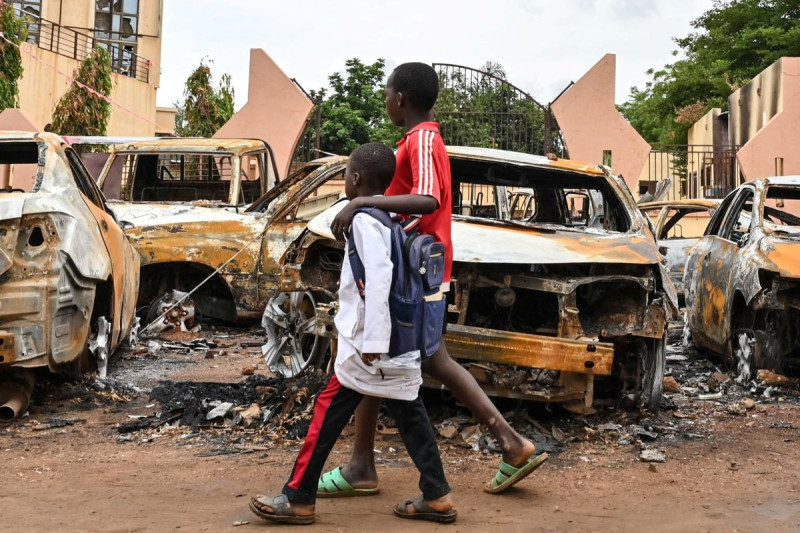 Niños pasan frente a los autos quemados frente a la sede del Partido Níger para la Democracia y el Socialismo del presidente Bazoum en Niamey.