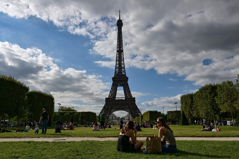 Turistas y parisinos se sientan en el Campo de Marte frente a la Torre Eiffel en París el 9 de agosto de 2023.