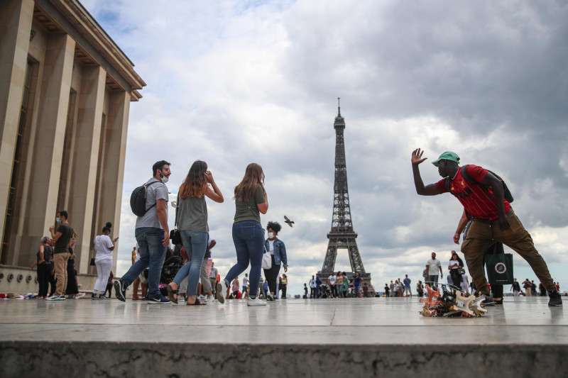 Un vendedor de souvenirs de la Torre Eiffel explica cómo tomarse una foto con la Torre Eiffel a una mujer, en la plaza Trocadero en París, Francia, el 14 de agosto de 2020.