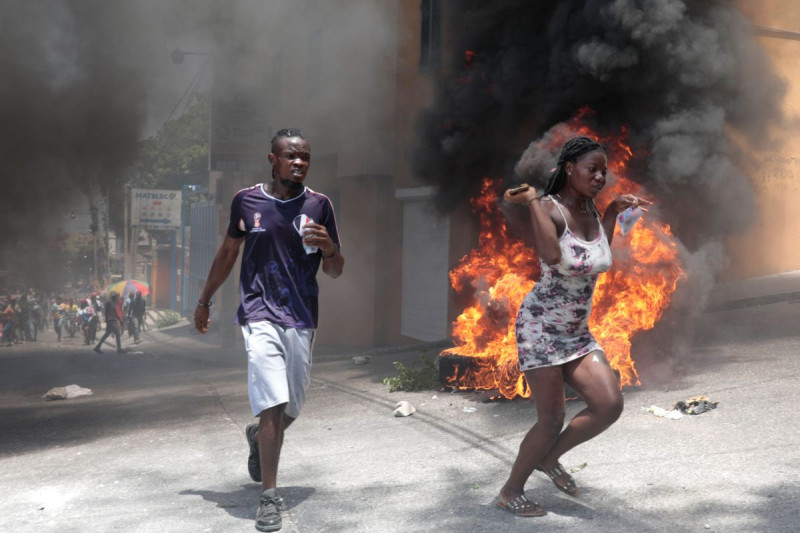 Manifestantes pasan corriendo junto a neumáticos incendiados durante una protesta contra la inseguridad, el 7 de agosto de 2023, en Puerto Príncipe, Haití.