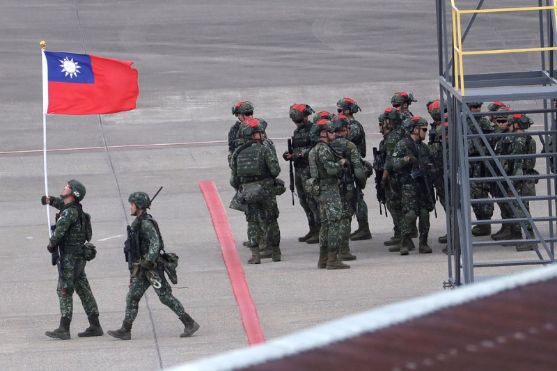 Un soldado taiwanés sostiene una bandera de Taiwán cerca de un grupo de soldados con marcas rojas en sus cascos.