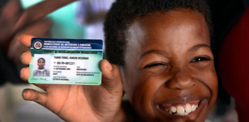 Un niño de origen haitiano ríe al lado de un carné entregado por las autoridades dominicanas a las personas que se han acogido al Plan Nacional de Regularización de Extranjeros Indocumentados.