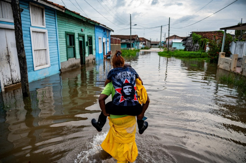 Un hombre carga a una mujer en su espalda mientras camina por el agua en un área inundada de Batabano